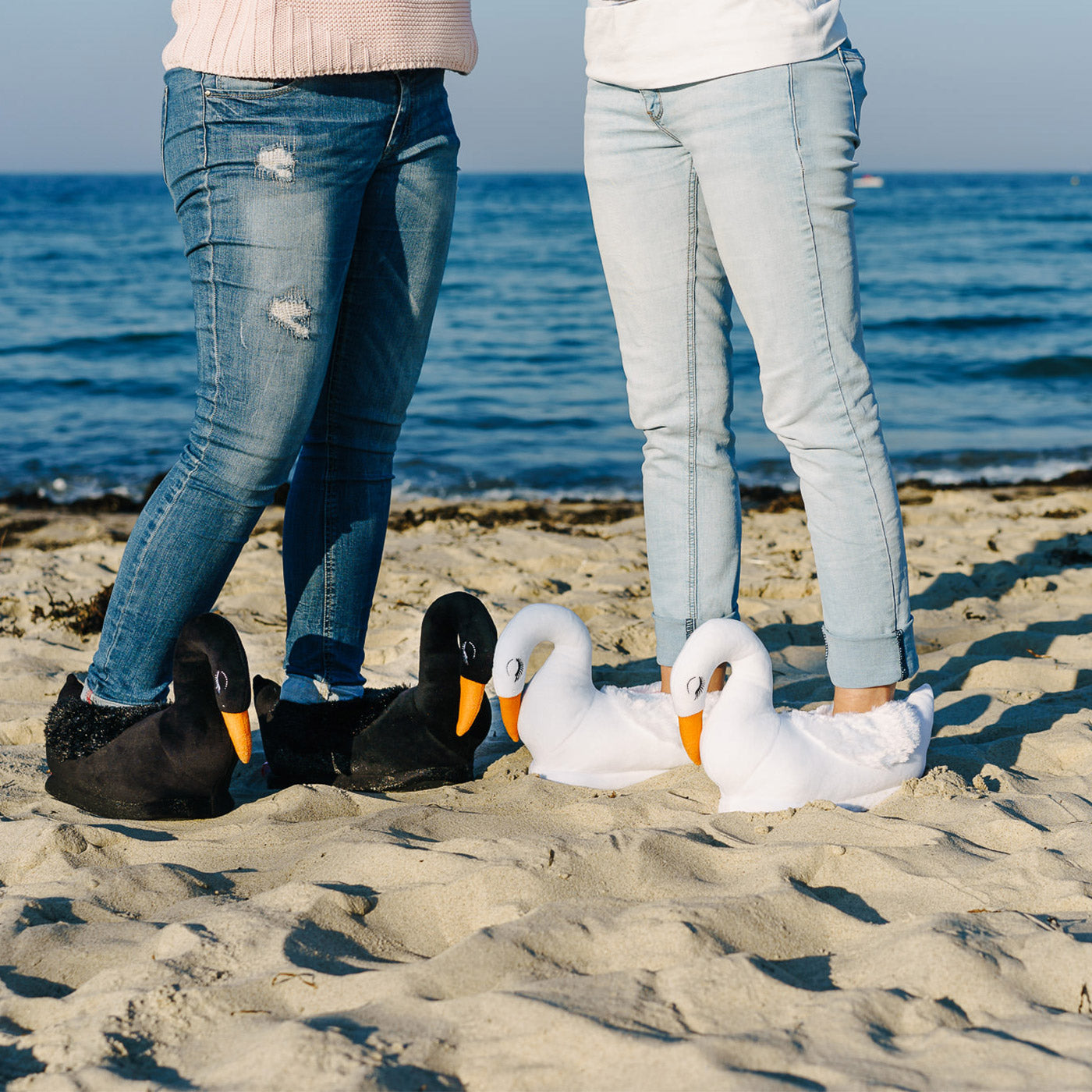 zwei Personen mit schwarzen und weissen Schwan Hausschuhen am Strand